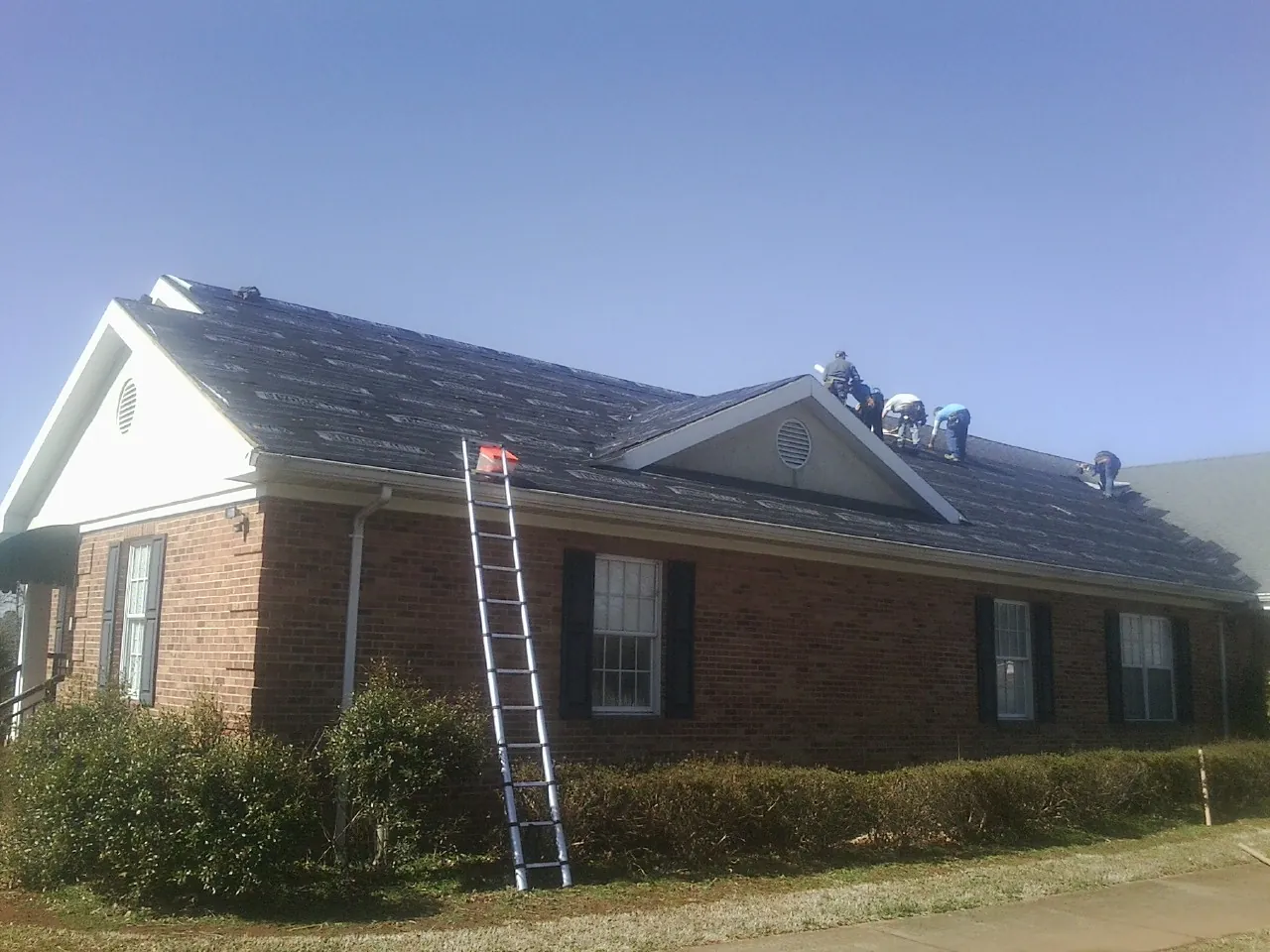 Crew tearing shingles off a brick ranch roof with a ladder set — Metal Roof Repair work by our crew in Crows Landing