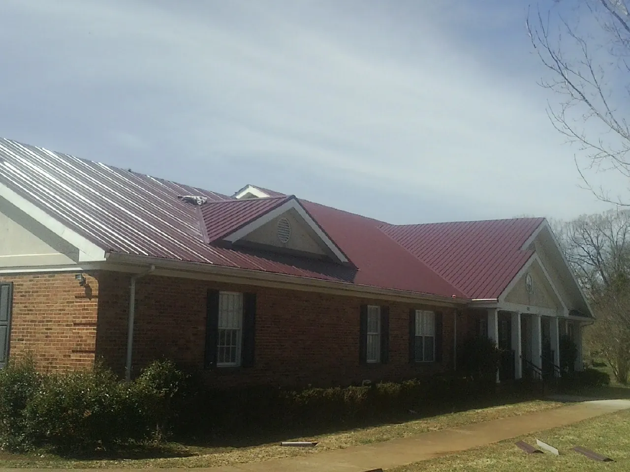 Red metal roof with gabled entries on a long brick building, from a Hail Damage Roof Repair job in Crows Landing